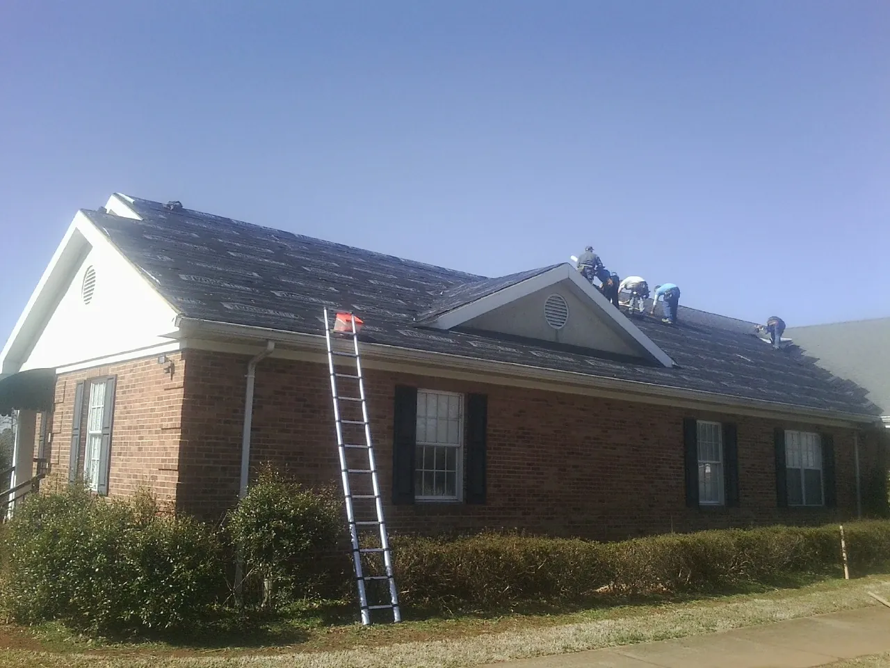 Crew tearing shingles off a brick ranch roof with a ladder set — Emergency Roof Repair work by our crew in Whippany