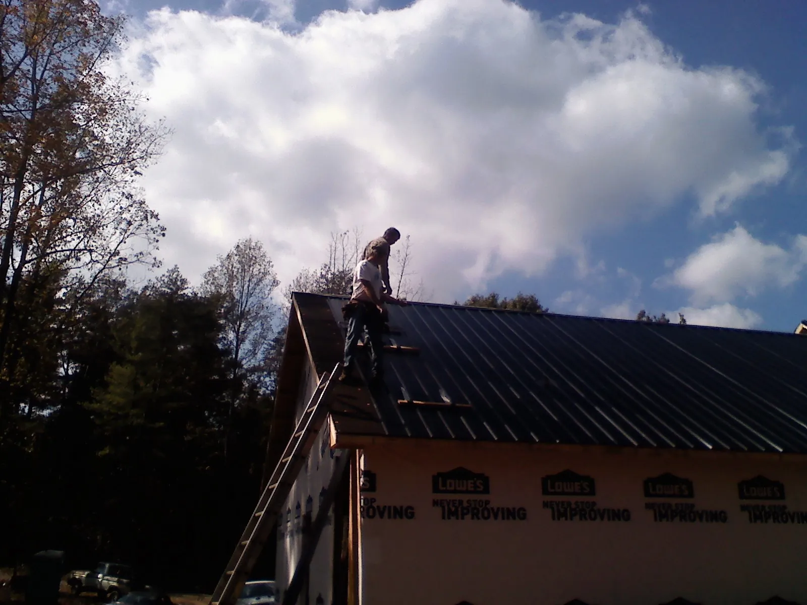 Roofer fastening dark metal panels high against a cloudy sky, from a Roof Inspection job in Whippany