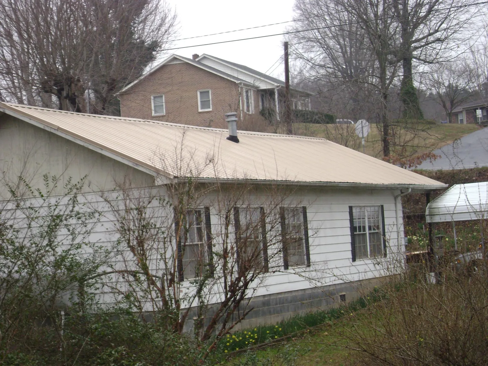 Tan metal roof on a white sided house set into a hillside — Commercial Roofing by Roofing Brothers in Whippany